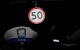 Wizerunek znaku ograniczenia prędkości do 50 kilometrów na godzinę. W tle widnieje policyjna czapka.