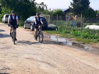 Dwóch policjantów na rowerach jadą po drodze szutrowej.