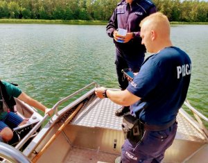 policjant rozmawiający z osobami korzystającymi ze sprzętu wodnego, w tym przypadku z łódki
