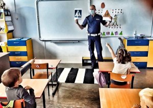 Policjant w maseczce pokazujący dzieciom w klasie znaki drogowe.