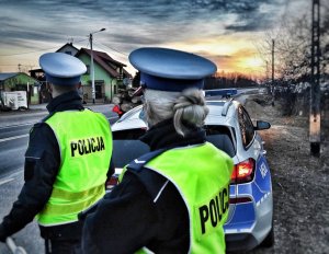 Policjanci ruchu drogowego, w tle radiowóz i zachodzące słońce